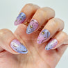 Nails with a gradient design of purple and pink, featuring gold accents on a white background.